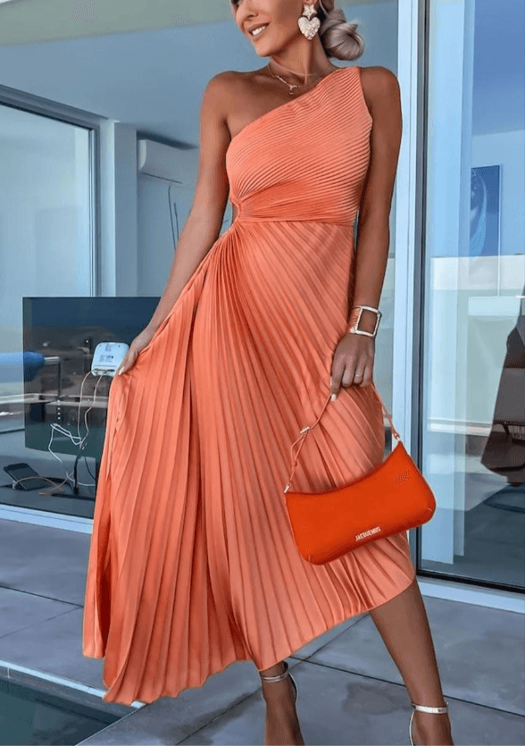 Lifestyle shot of a woman in the fuchsia Ainsley one-shoulder pleated midi dress, walking and showing movement of the skirt.