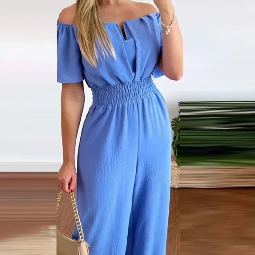 Front view of a woman wearing a light blue off-shoulder jumpsuit, posing elegantly.