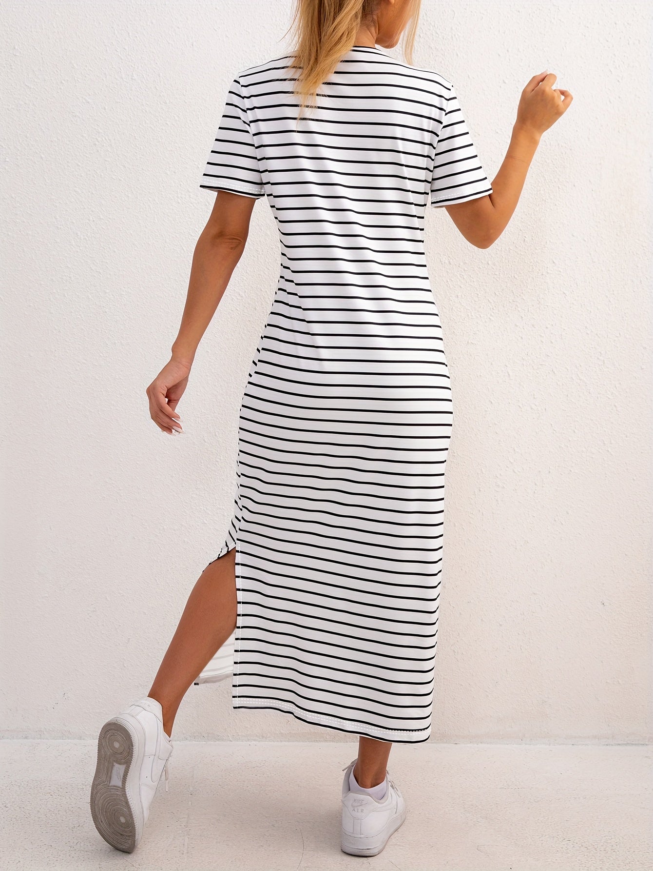 Side profile of a woman showcasing the elegant side split on the striped jersey midi dress, enjoying a sunny day.
