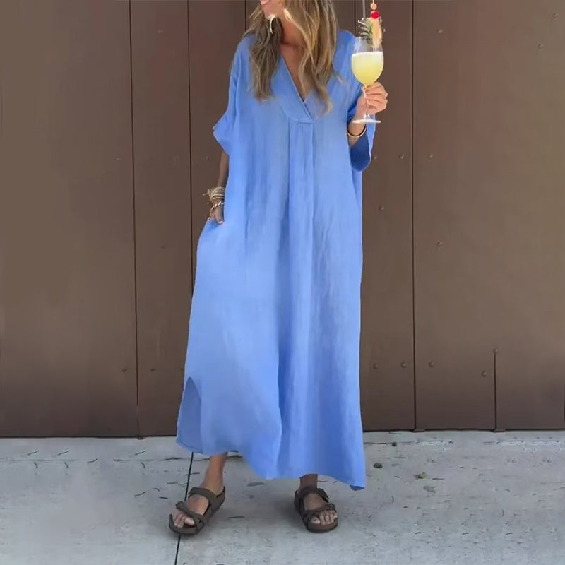 Front view of a woman wearing a blue Aurora casual V-neck dress, standing outdoors in a relaxed pose.