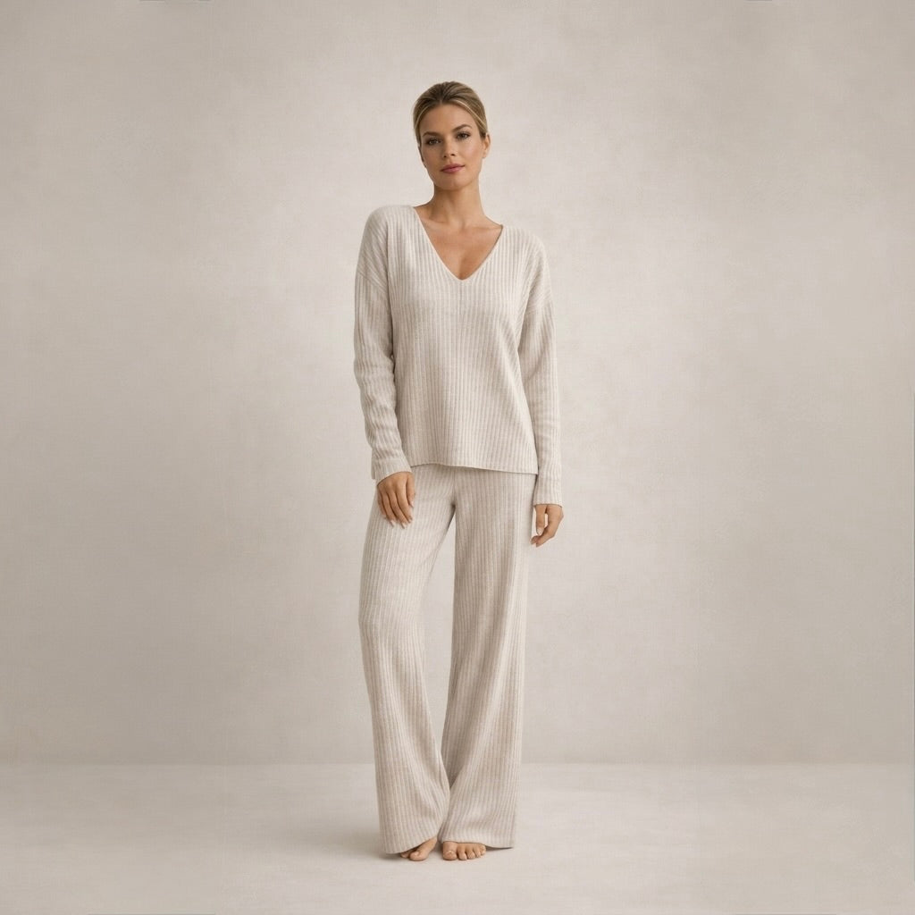 A woman wearing a complete beige cozy knit loungewear set, standing with a slight smile, showcasing the relaxed fit and ribbed texture.