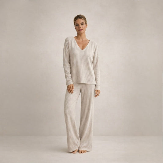A woman wearing a complete beige cozy knit loungewear set, standing with a slight smile, showcasing the relaxed fit and ribbed texture.