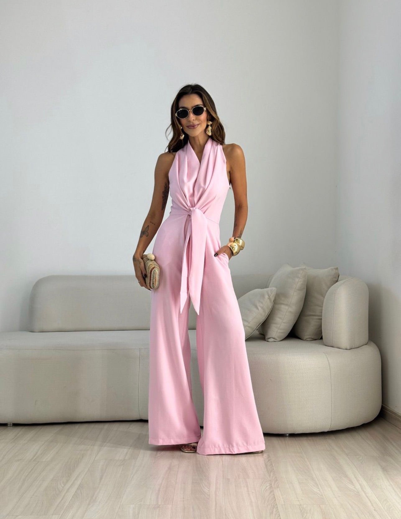 Beige wide-leg halterneck jumpsuit styled with heels and a clutch for an evening look.