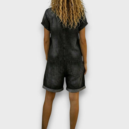 Woman sitting comfortably in a black denim jumpsuit, highlighting the ease of movement and relaxed fit.