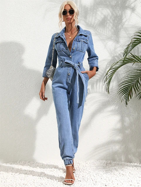Young woman smiling, wearing a light wash denim jumpsuit with a belt, walking outdoors.